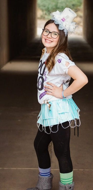 Girl in a DIY 2020 costume with a toilet paper top hat, a T-shirt covered in 2020 references, a skirt made of face masks and mismatched socks