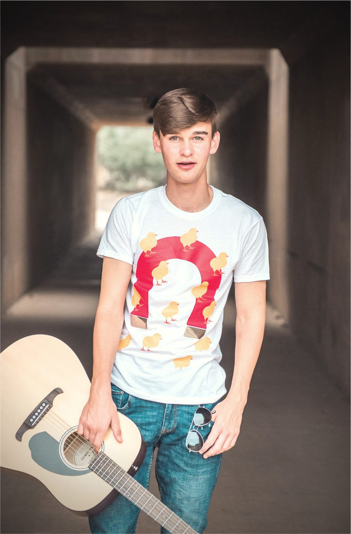 Teen boy in a white T-shirt with a red magnet and little chicks on it, holding a guitar