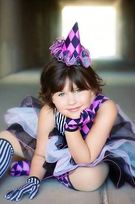 Girl in a pink and purple harlequin clown costume with a pointed hat, sitting in a tunnel