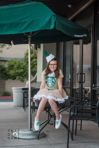 Girl in a DIY Frappuccino costume sitting at a cafe table under a green Starbucks umbrella