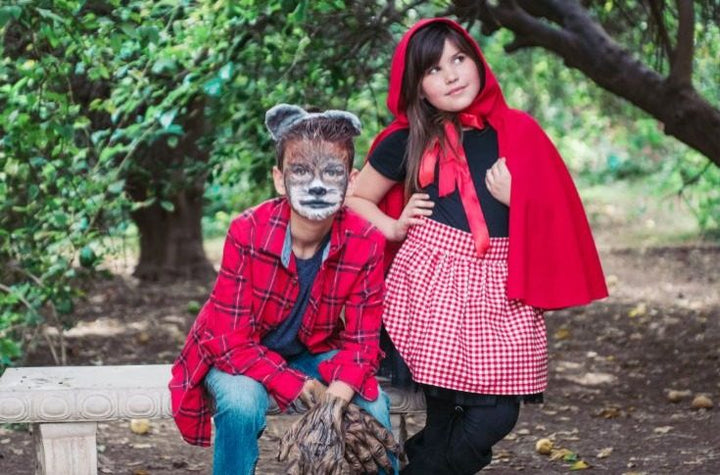A girl in a red cape and gingham skirt as Little Red Riding Hood next to a boy with wolf ears and face paint as the Big Bad Wolf