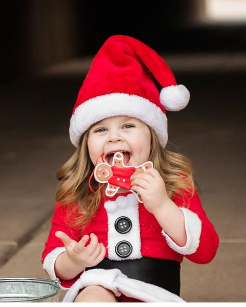 Toddler in a Santa costume eating a gingerbread cookie