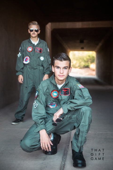 Two teen boys in green flight suits with patches and aviator sunglasses, dressed as Maverick and Goose from Top Gun, in a tunnel