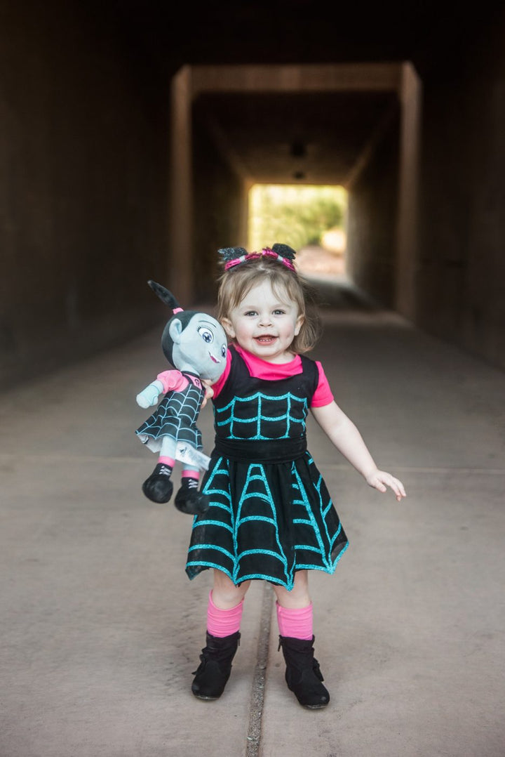 Toddler in a DIY Vampirina costume with a spiderweb dress, holding a Vampirina doll in a tunnel